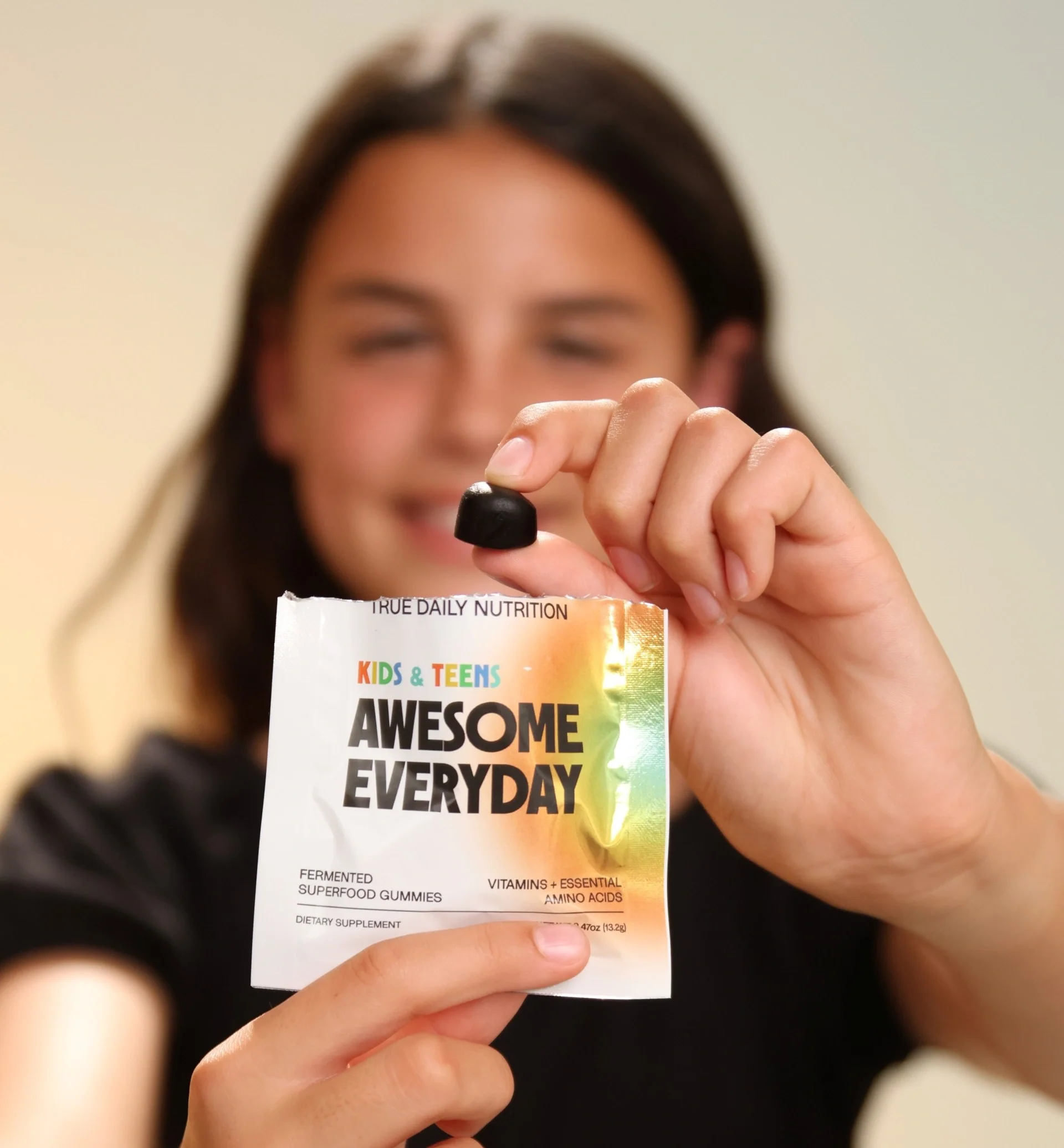 Child holding an Awesome Everyday™ Kids & Teens gummy and product packet.