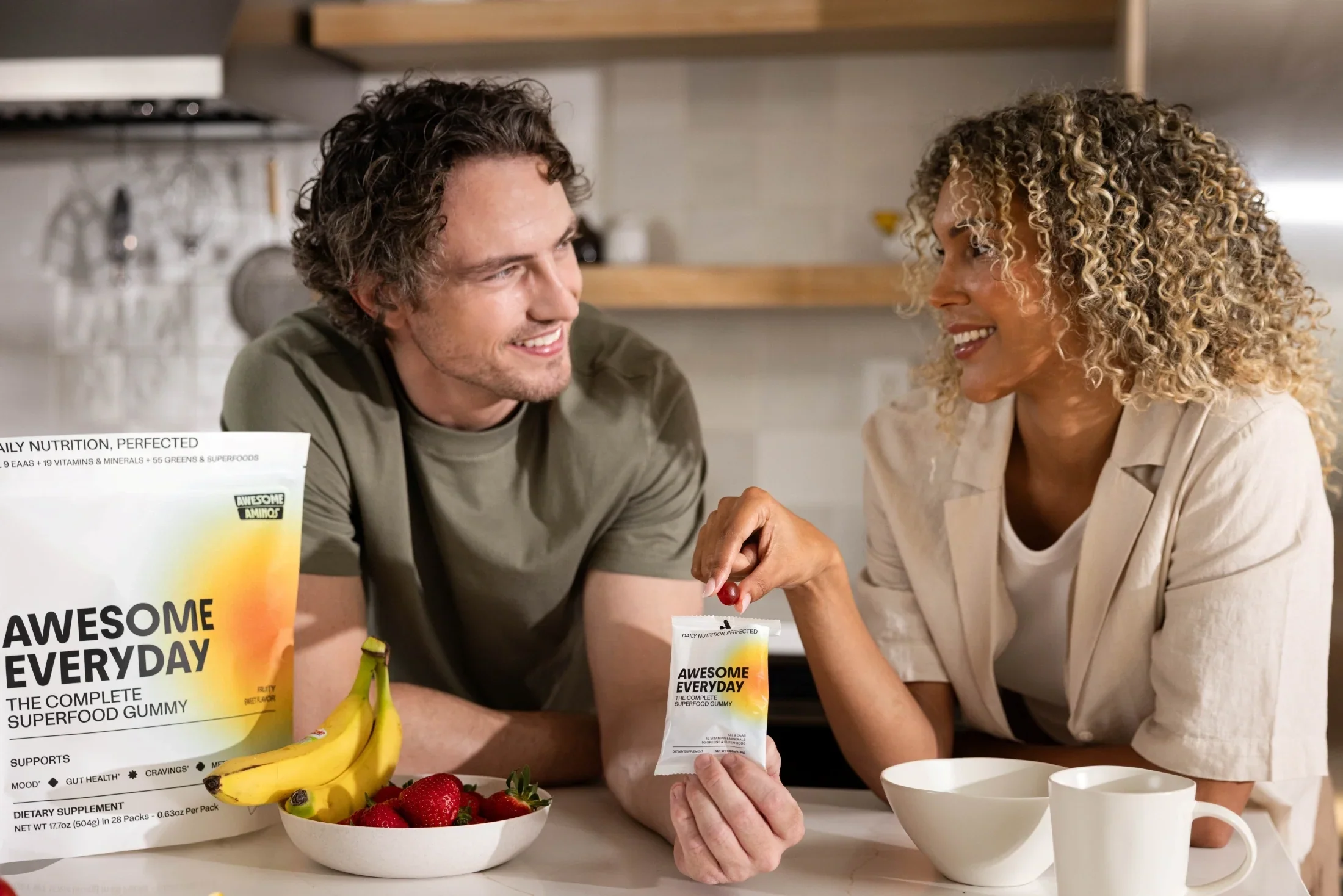 Couple holding an Awesome Everyday™ gummy pouch with fruit sitting on a table.