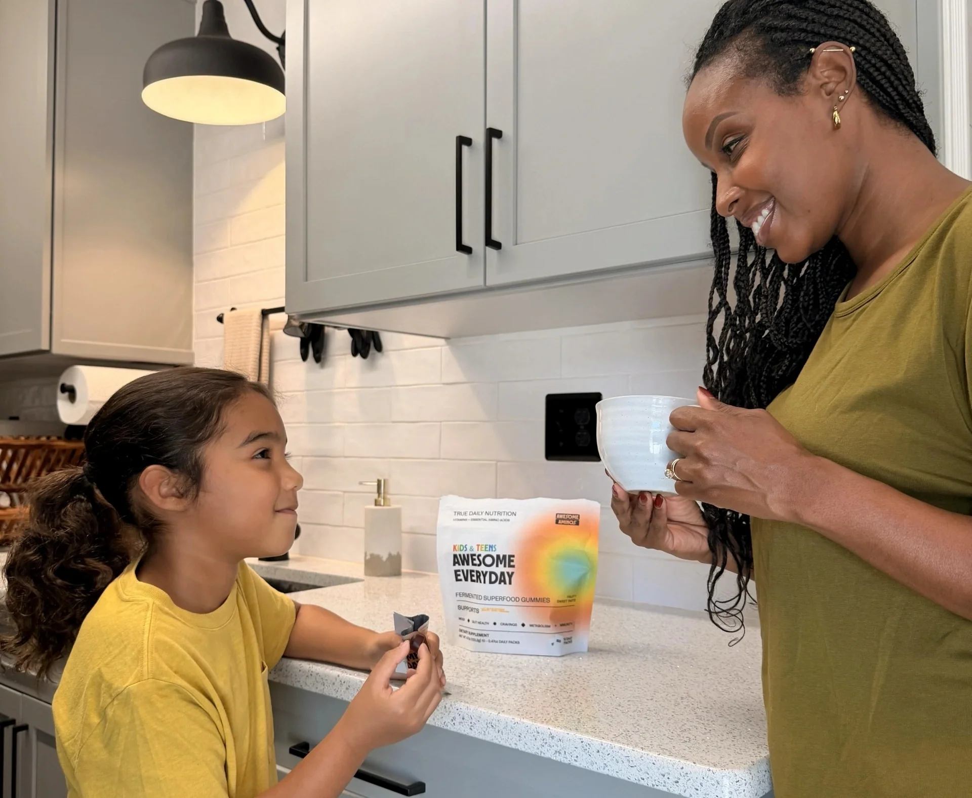 Child eating Awesome Everyday™ Kids & Teens gummies with a parent in the kitchen.