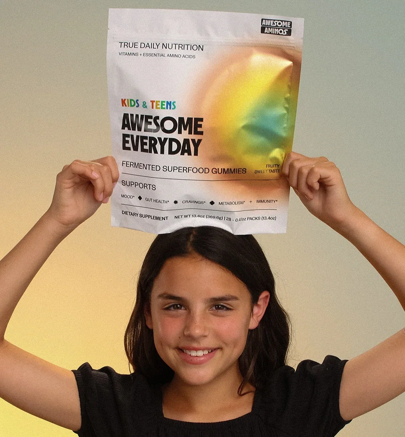 Smiling child holding an Awesome Everyday™ Kids & Teens gummy pouch.