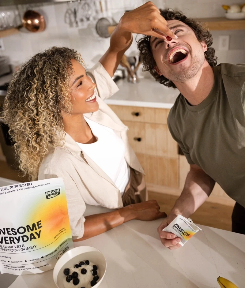 Couple sharing an Awesome Everyday™ gummy beside the product pouch in a bright kitchen.